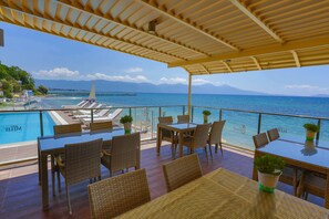Una terraza con piscina, zona de comedor y vista al océano.