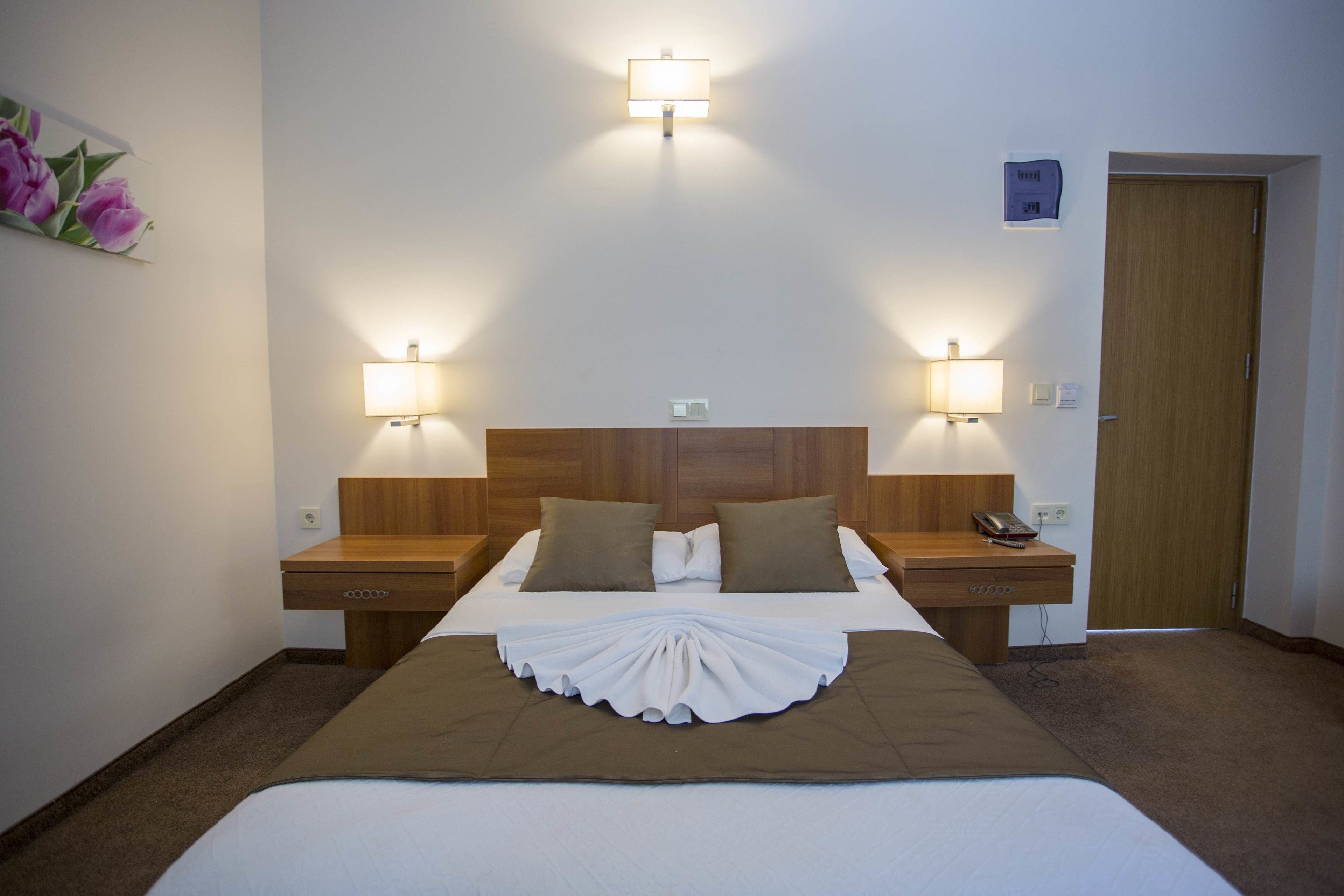 Habitación de hotel con una cama grande, dos mesitas de noche, un cabecero de madera y dos lámparas de pared.