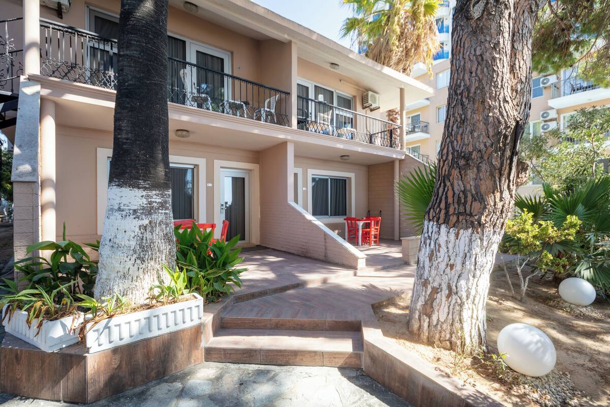 Un hotel de varios pisos con una escalera central, asientos exteriores y una palmera.