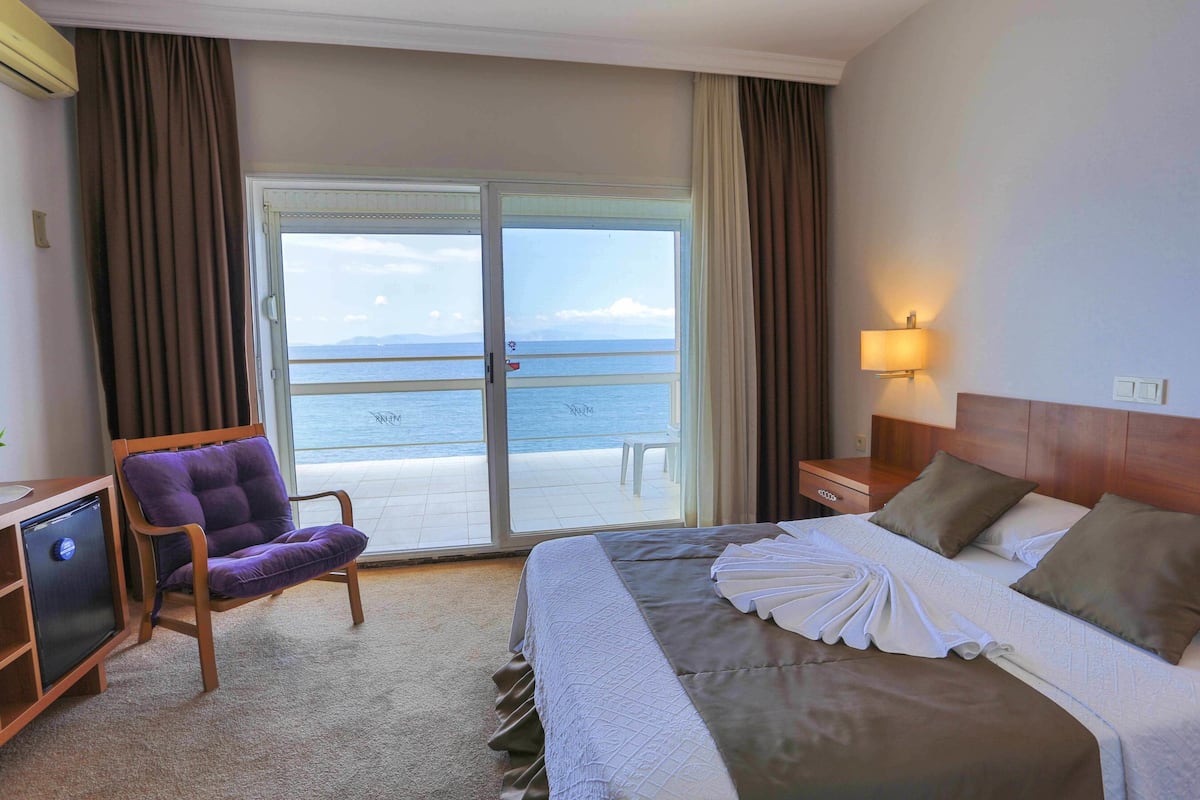 Habitación de hotel con cama, una silla, un escritorio y vista al mar a través de una puerta corrediza.
