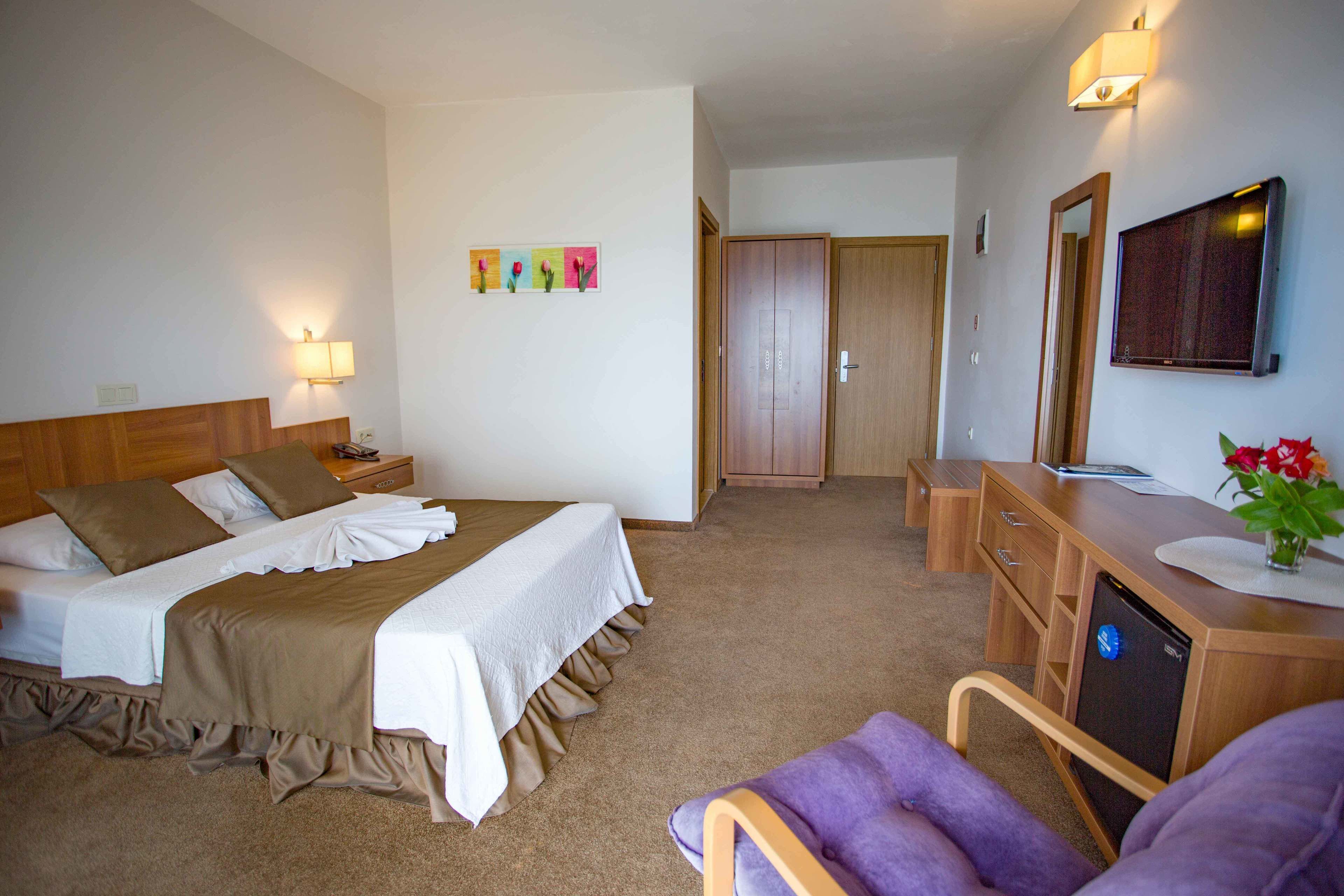 A hotel room with a bed, bedside table, lamp, desk, chair, and a mirror.