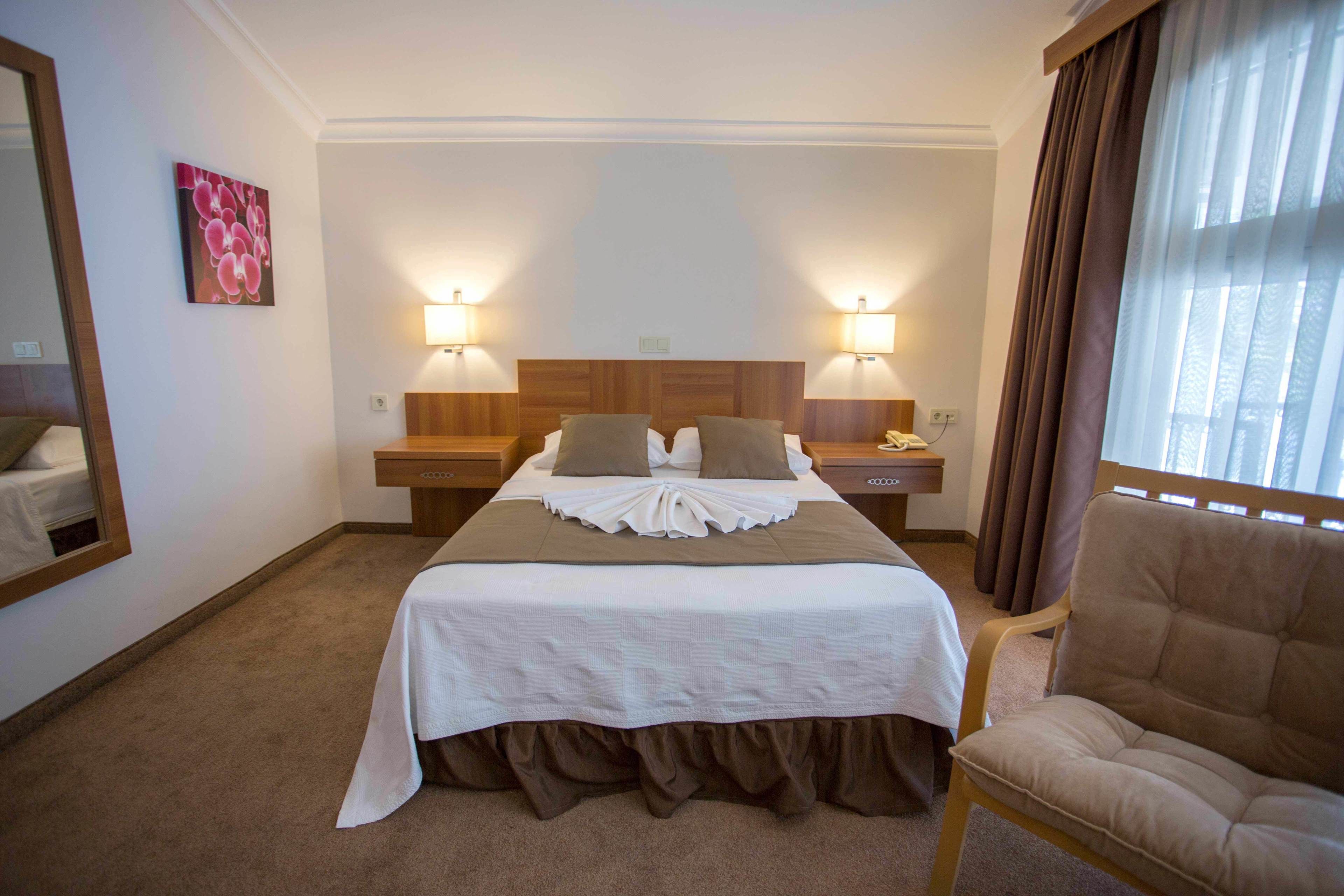 A hotel room with a large bed, two bedside lamps, a chair, a mirror, and a painting on the wall.
