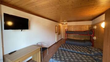 A compact room with a bunk bed, a desk, and a flat-screen TV mounted on the wall.