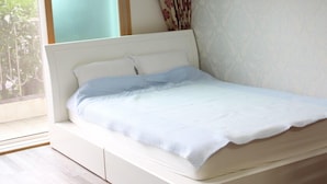 A neatly made bed with a white headboard and a light blue blanket. - Memory Tour (Seogwipo)