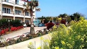 A multi-story building with balconies, a parking area, and a variety of plants and flowers. - Memory Tour (Seogwipo)