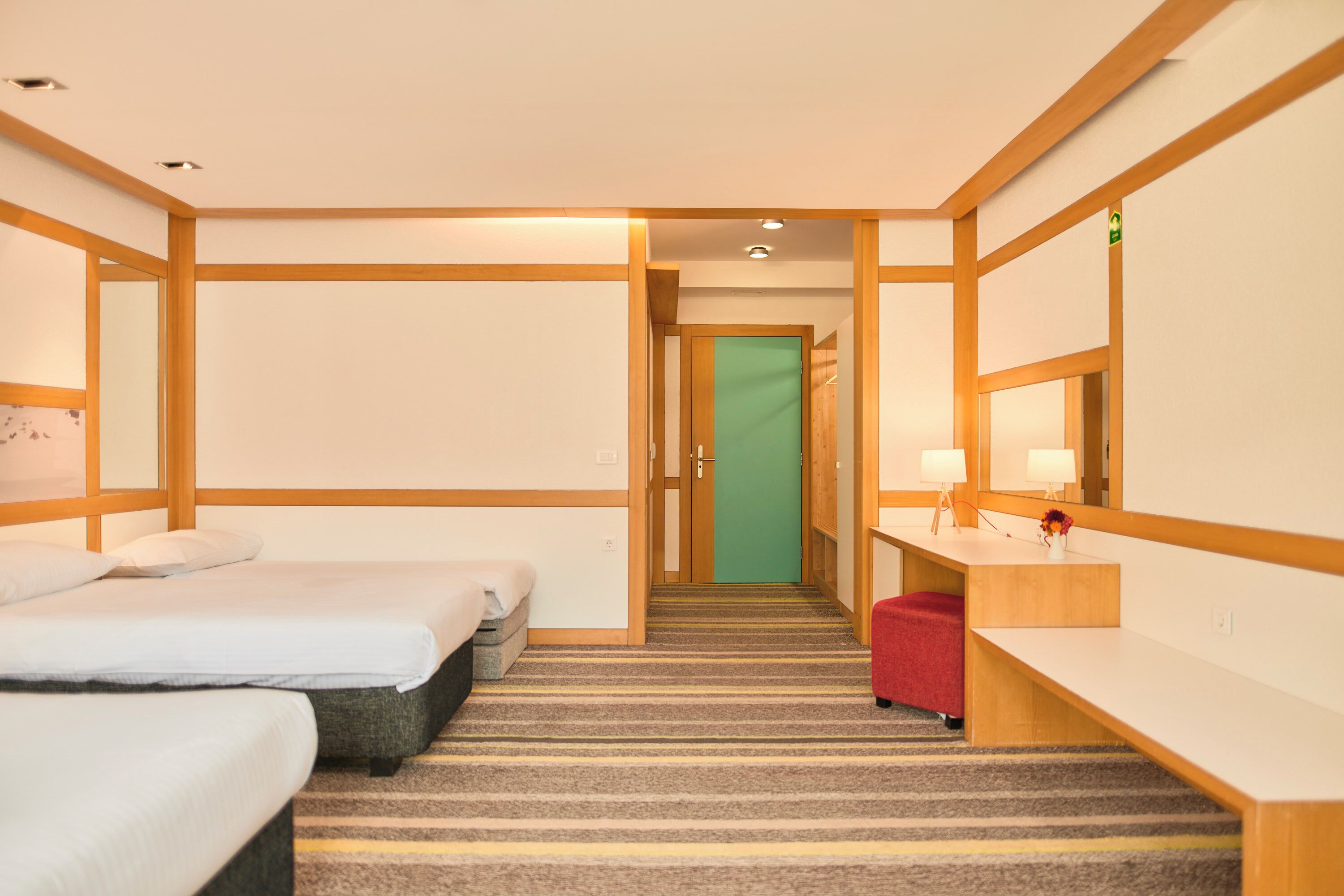 A hotel room with two beds, a desk with a lamp, a mirror, and a carpeted floor.
