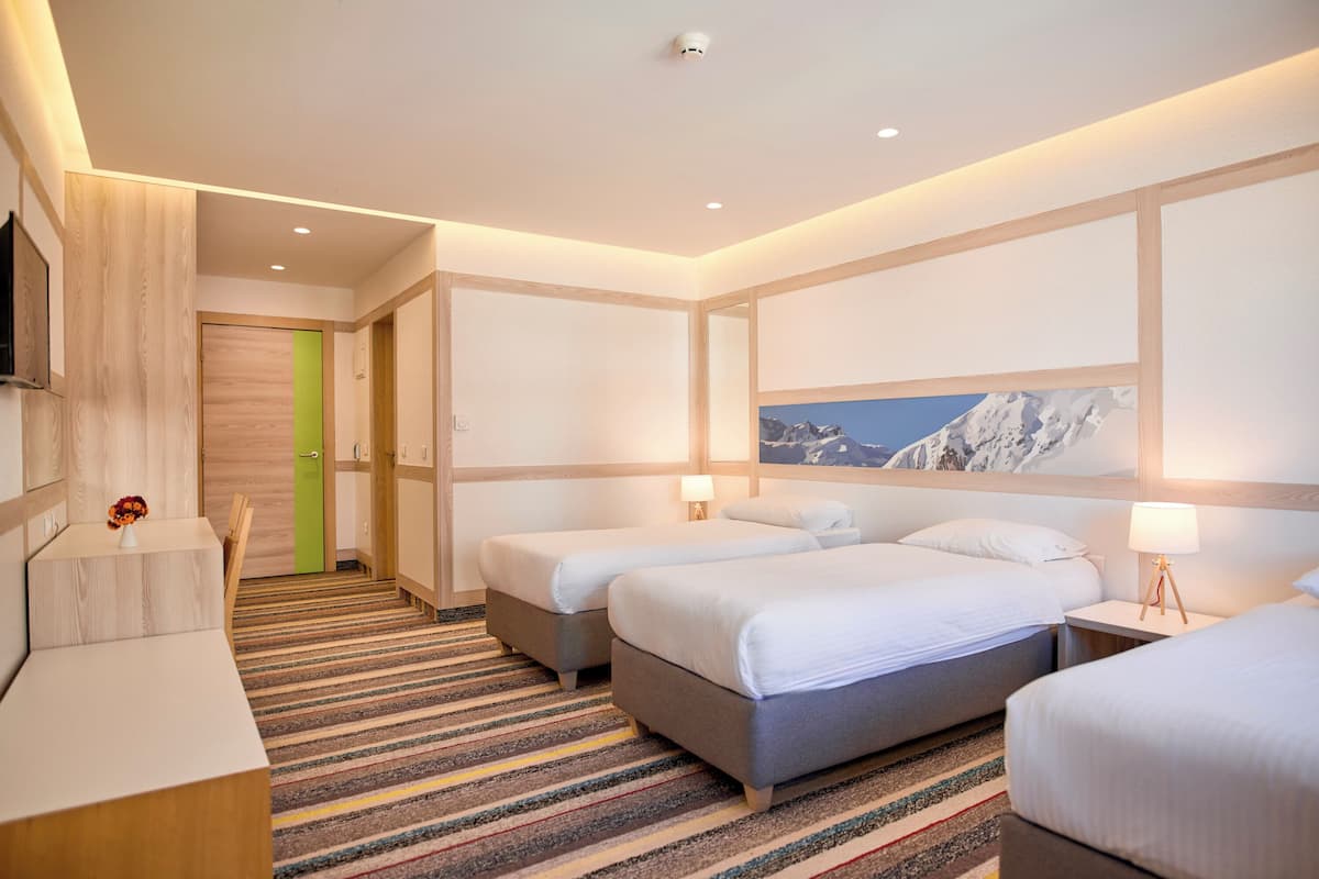A hotel room with two beds, a desk, a TV, and a green door.