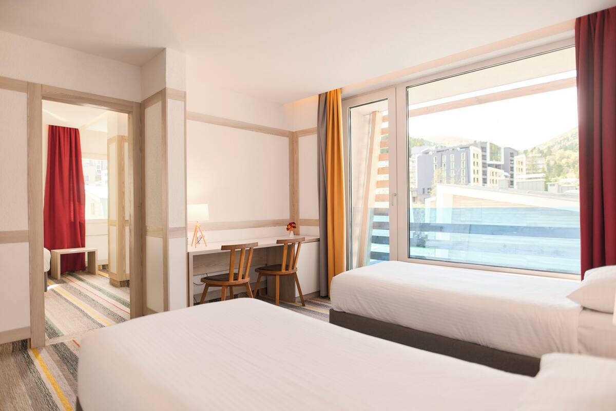 A hotel room with two beds, a desk, and a view of the city.