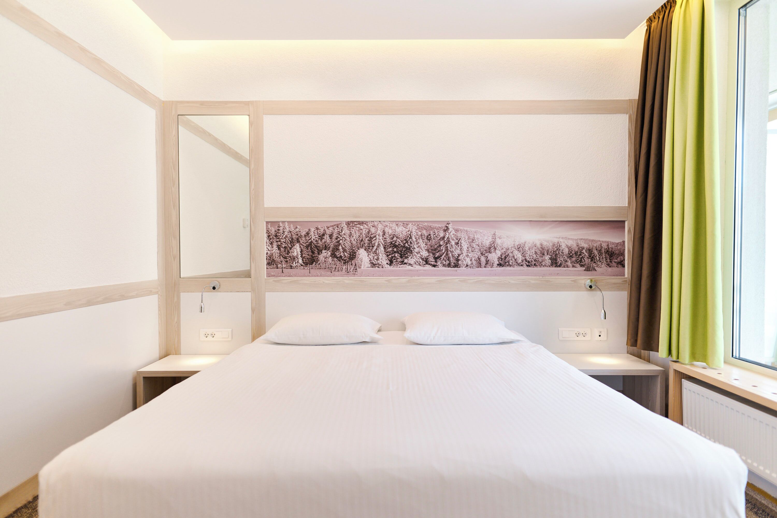 A hotel room with a large bed, a nightstand, a mirror, and a window with curtains.