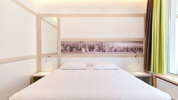 A hotel room with a large bed, a nightstand, a mirror, and a window with curtains.