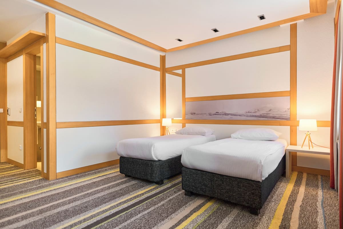 A hotel room with two beds, a large painting on the wall, and a striped carpet.