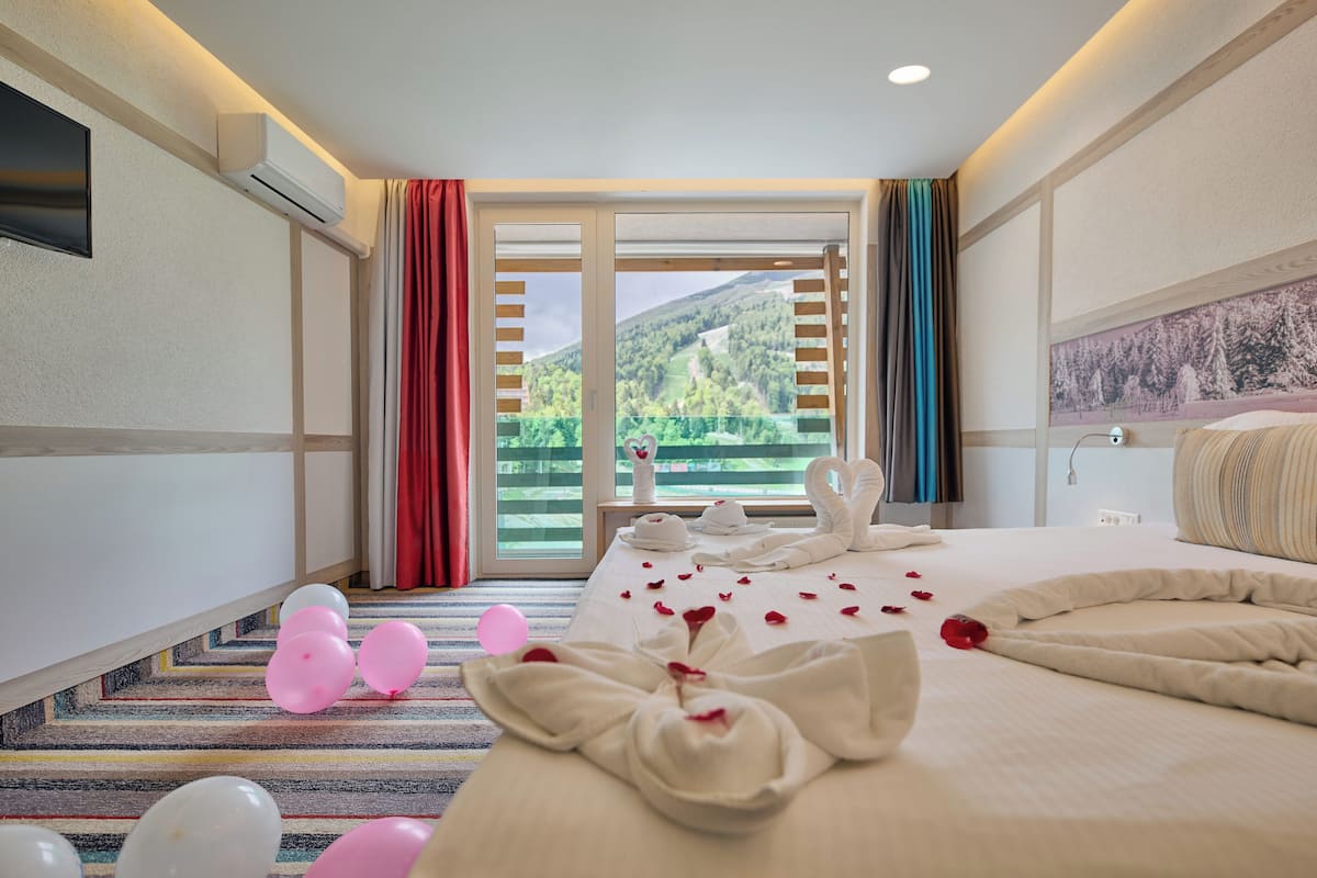 A hotel room with a bed, a window with curtains, a flat-screen TV, and a wall-mounted air conditioner.