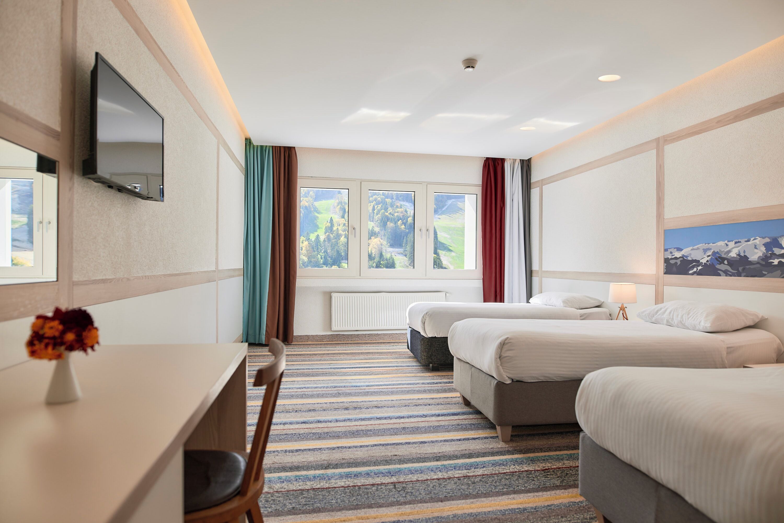 Una habitación de hotel con dos camas, un escritorio, un televisor y una ventana con cortinas.