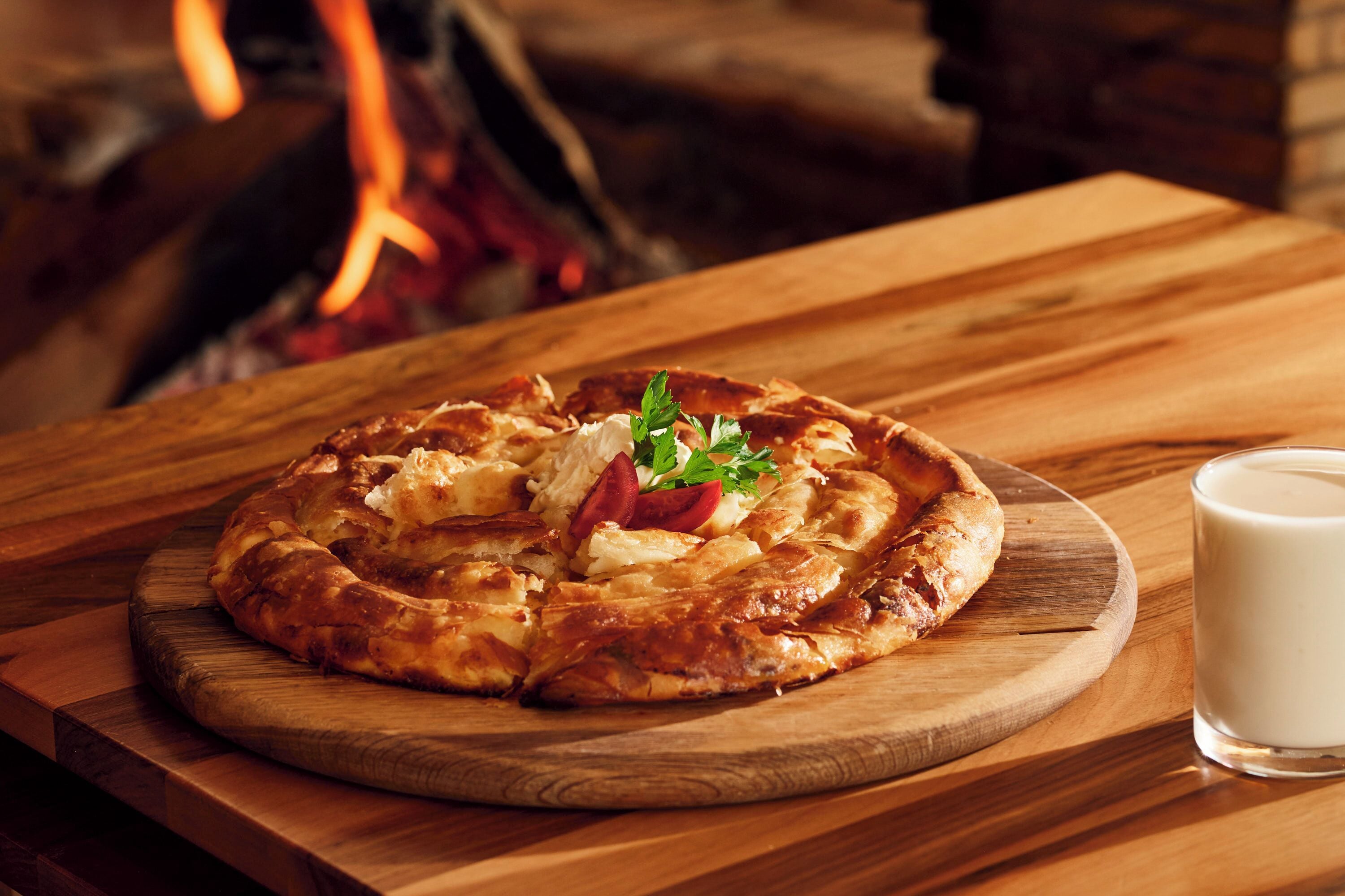 Uma pizza sobre uma tábua de madeira, com um copo de leite ao lado.
