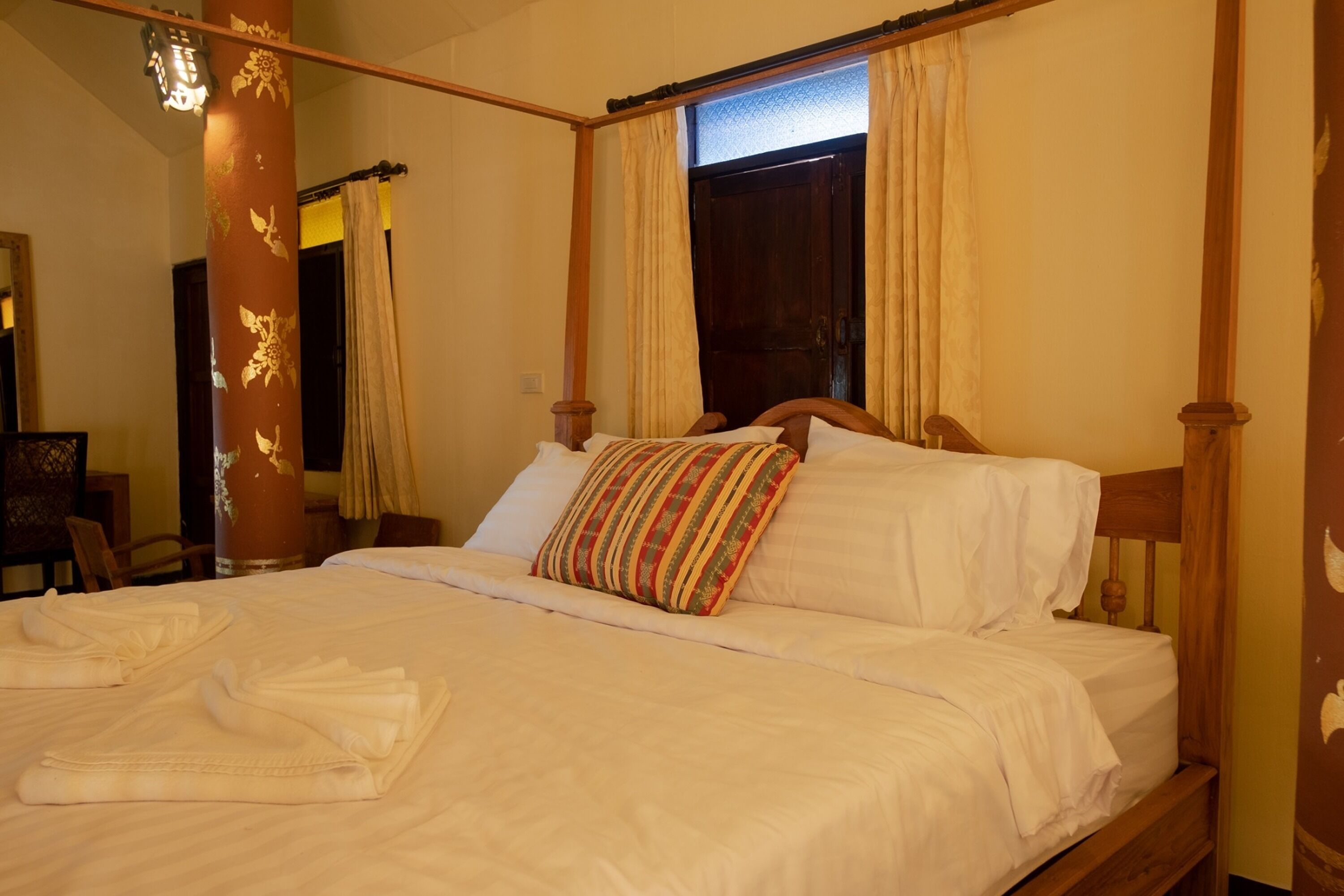 A four-poster bed with white linens and a colorful striped pillow.