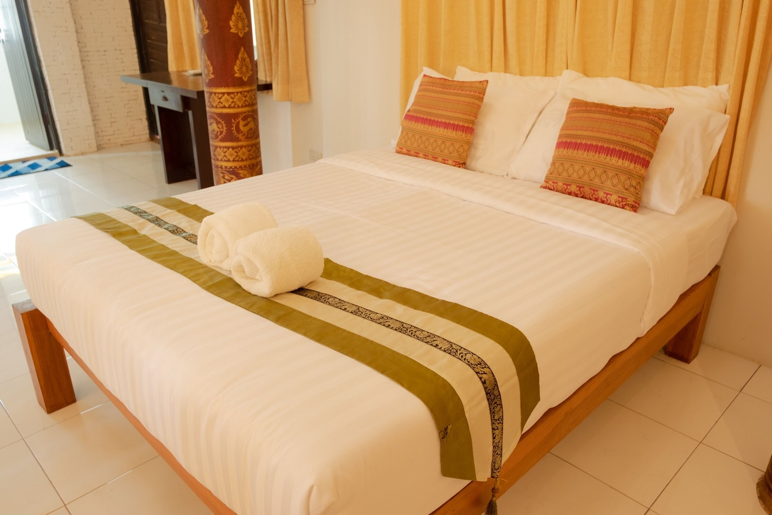 Una cama bien hecha con una colcha blanca y verde a rayas, dos almohadas y una toalla enrollada.