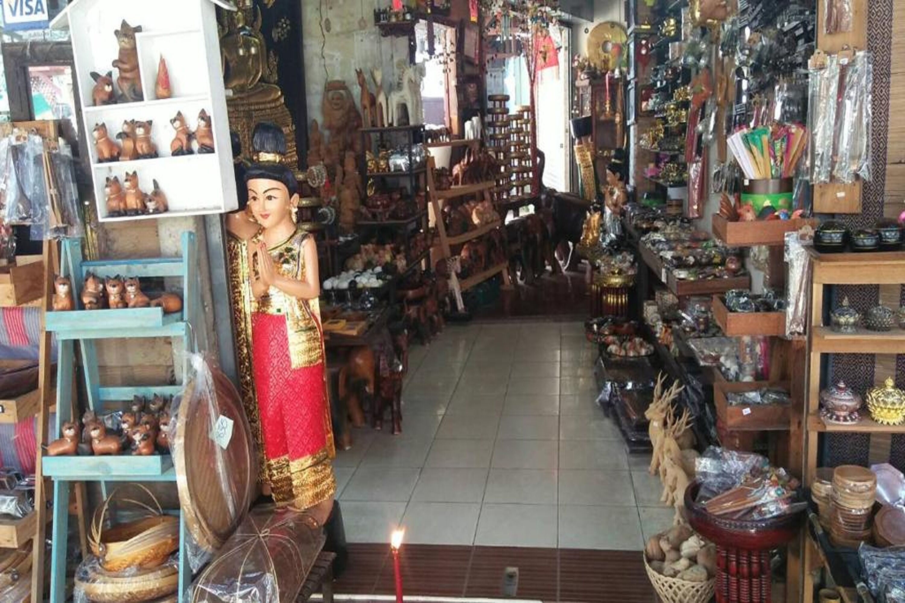 A narrow, cluttered shop with various items on shelves and tables, including figurines and pottery.