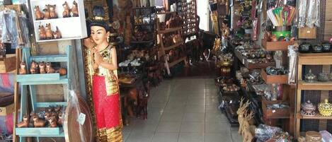 A narrow, cluttered shop with various items on shelves and tables, including figurines and pottery.