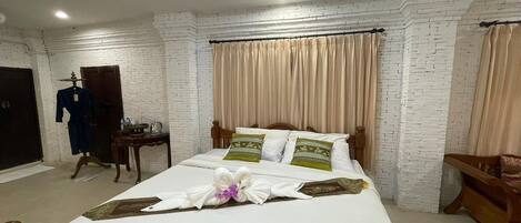 Habitación de hotel con pared de ladrillo blanco, cama con almohadas verdes y blancas, mesita de noche de madera y una silla de madera.