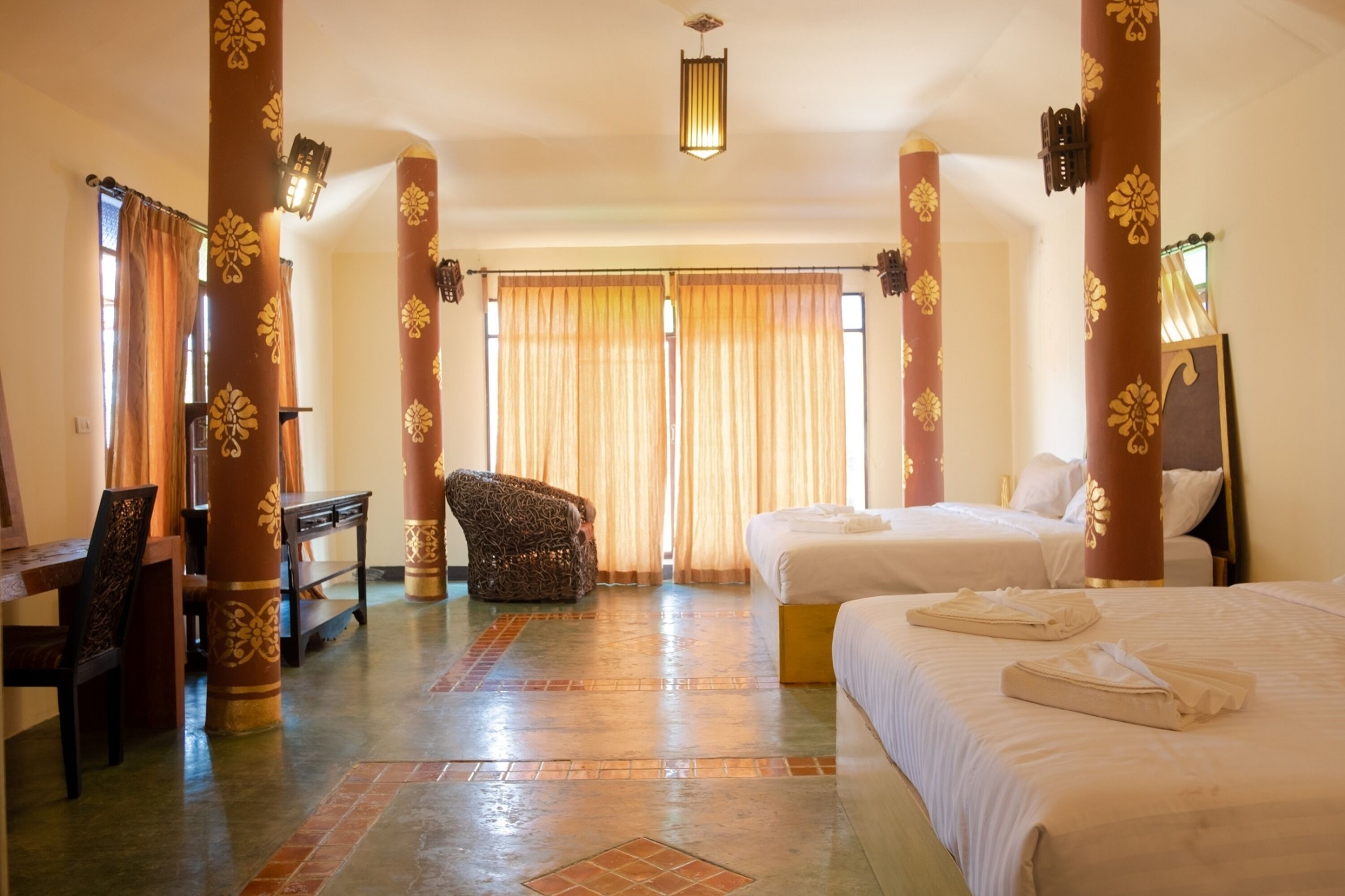 Une chambre d’hôtel avec deux lits, un bureau, une chaise et une grande fenêtre avec des rideaux.