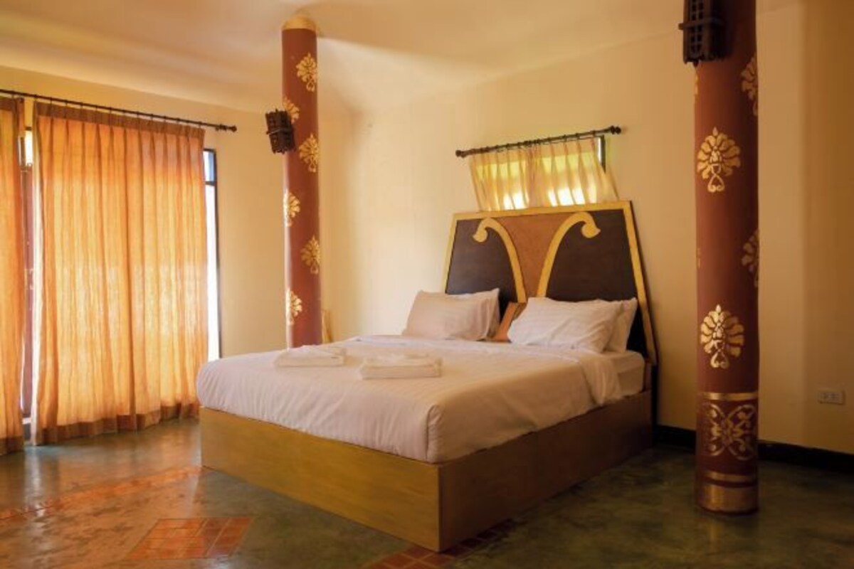 A single bed with a wooden headboard and a canopy, a large window with curtains, and a patterned pillar.