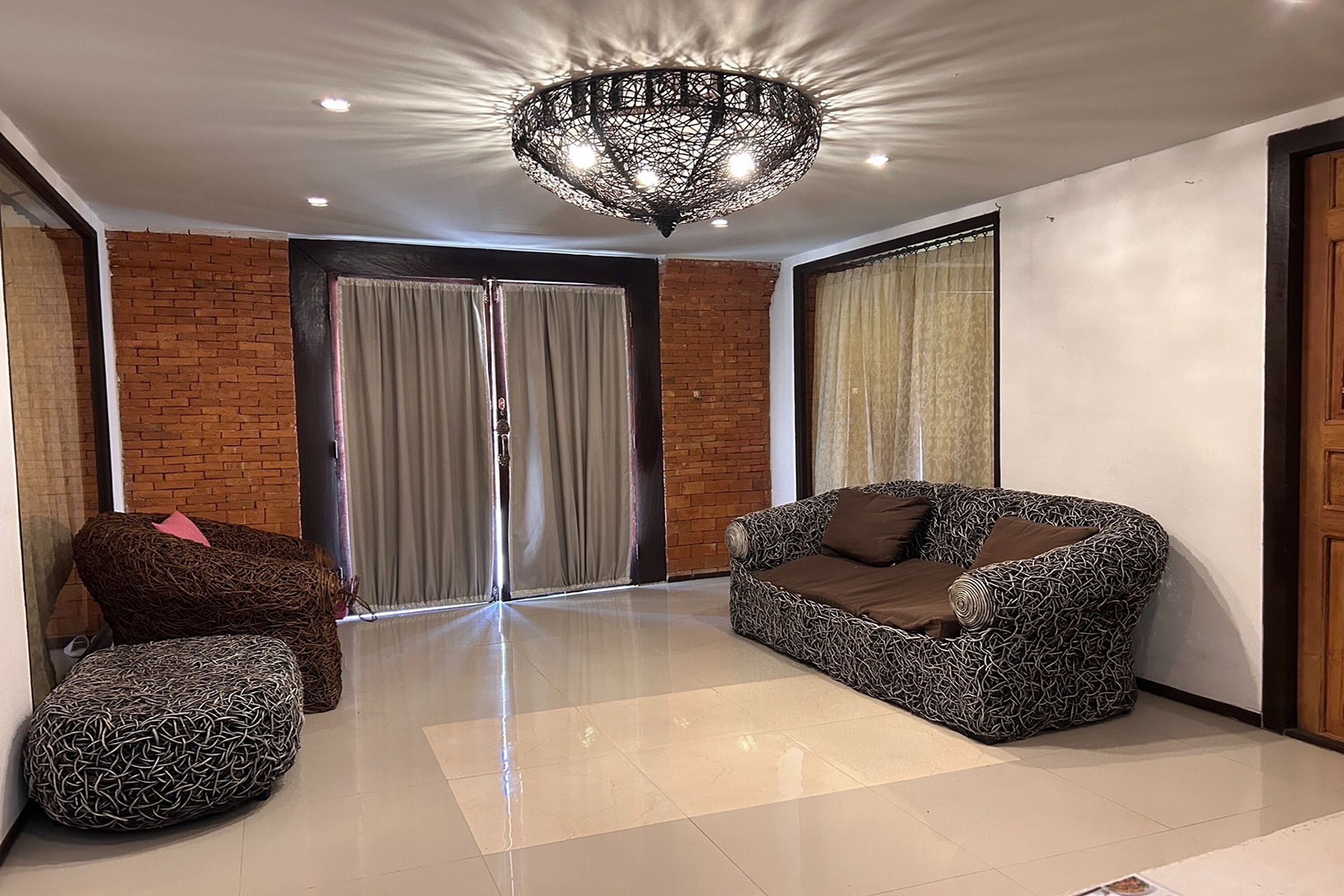 Un vaste espace de vie agrémenté d’un canapé à motifs, d’un pouf et d’un lustre moderne.