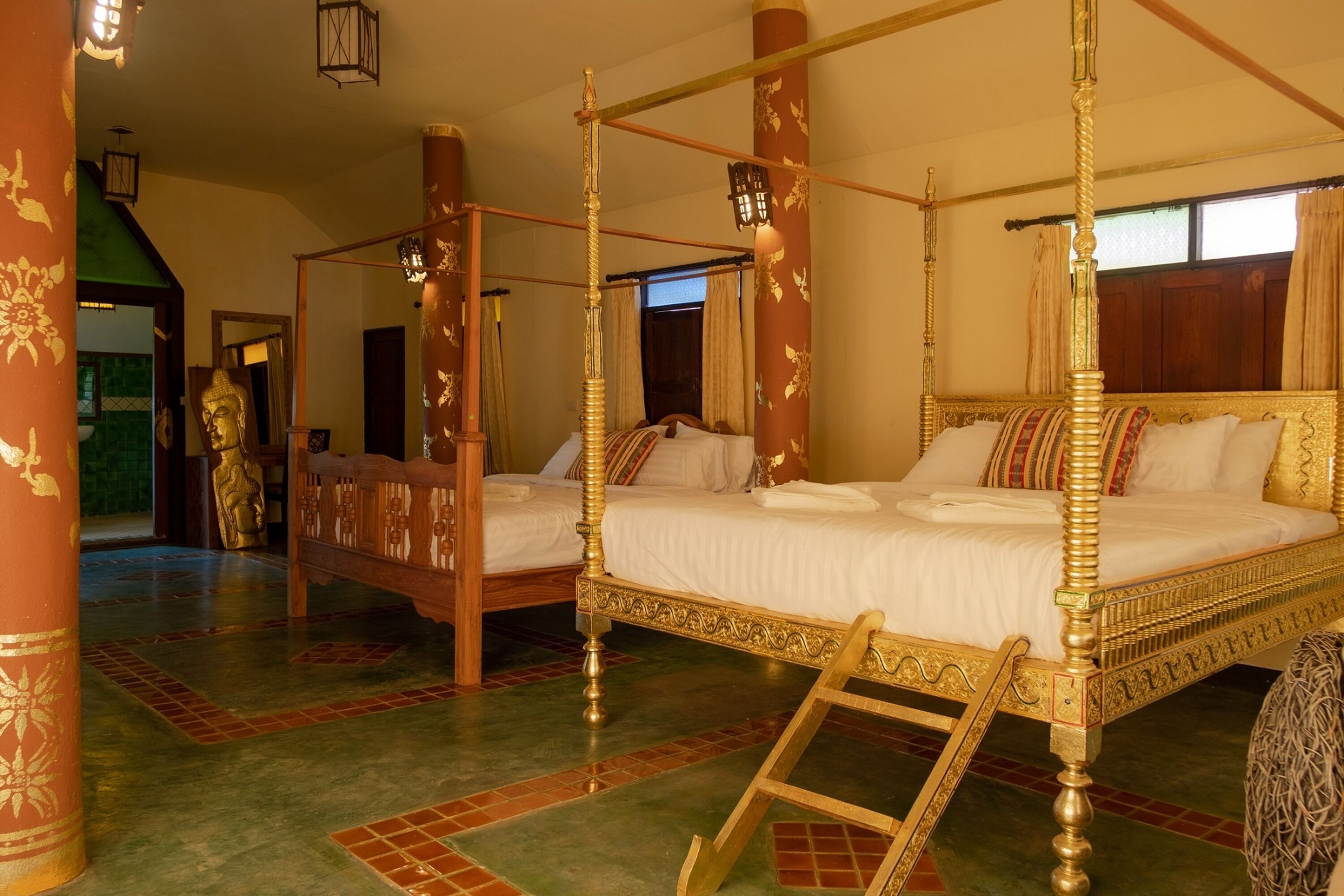 A four-poster bed with a golden frame, a wooden ladder, and a large Buddha statue in the background.