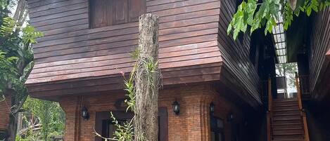 Une maison traditionnelle en bois, dotée d’un toit à pente, d’un escalier menant à l’étage supérieur et de deux chaises blanches dans le jardin.