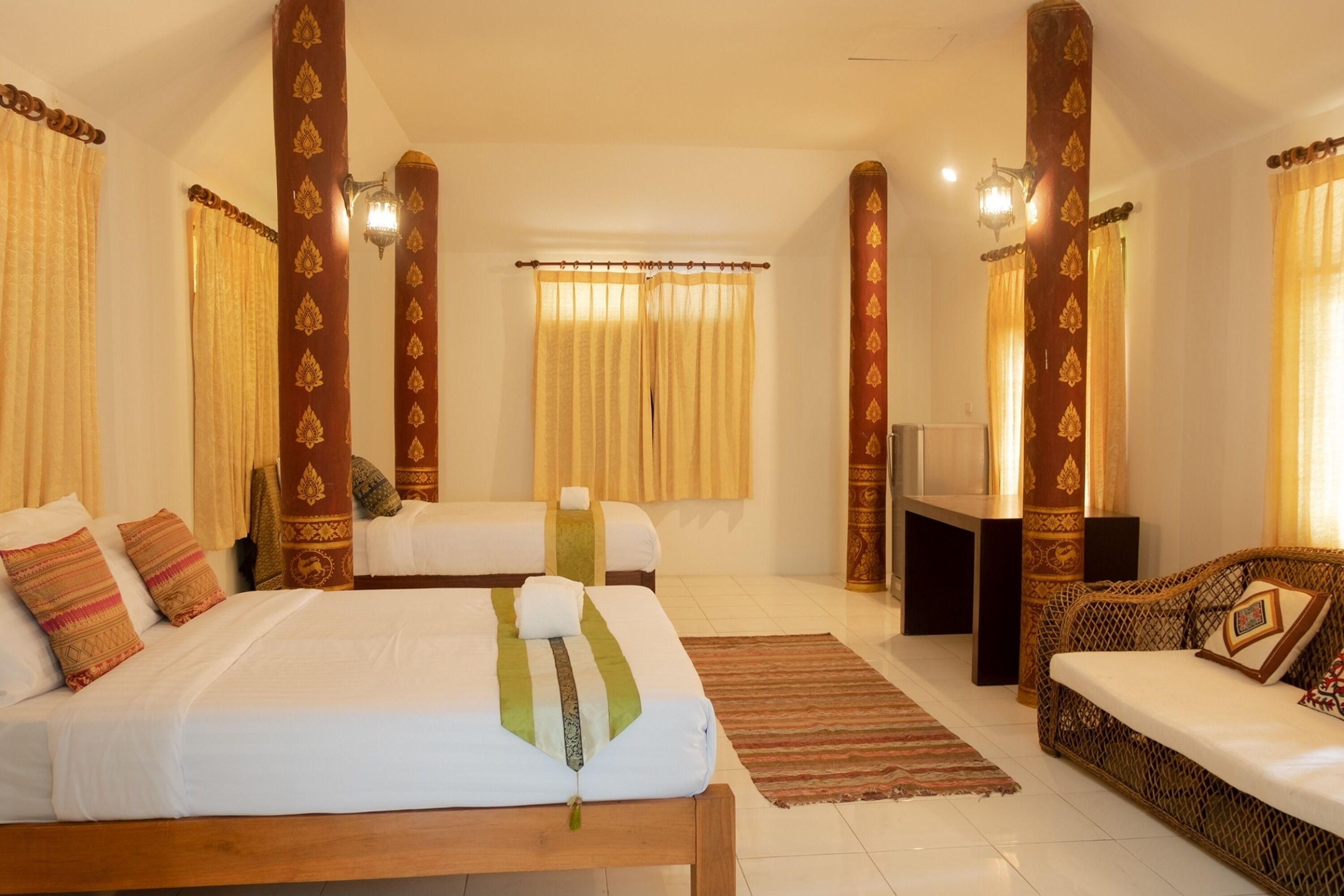 A hotel room with two beds, a sofa, a TV, and decorative pillars.