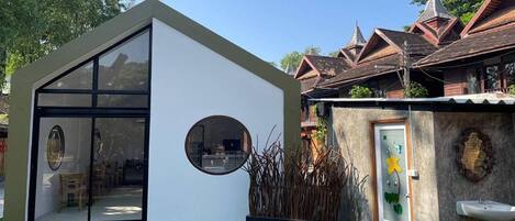 A modern house with a glass door, a small garden, and a traditional wooden structure in the background.