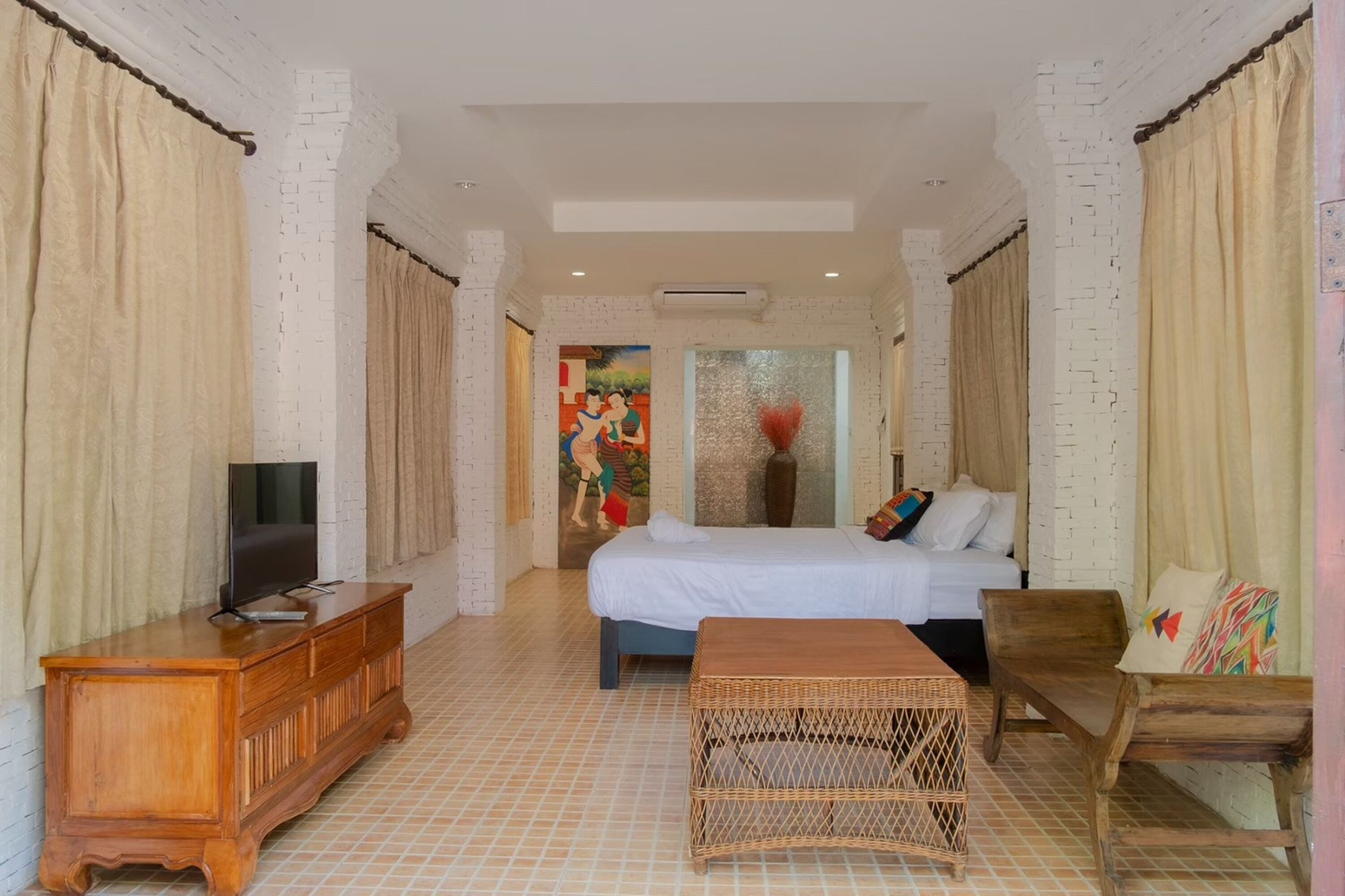 A hotel room with a bed, a television on a wooden dresser, a wicker table, and a chair.