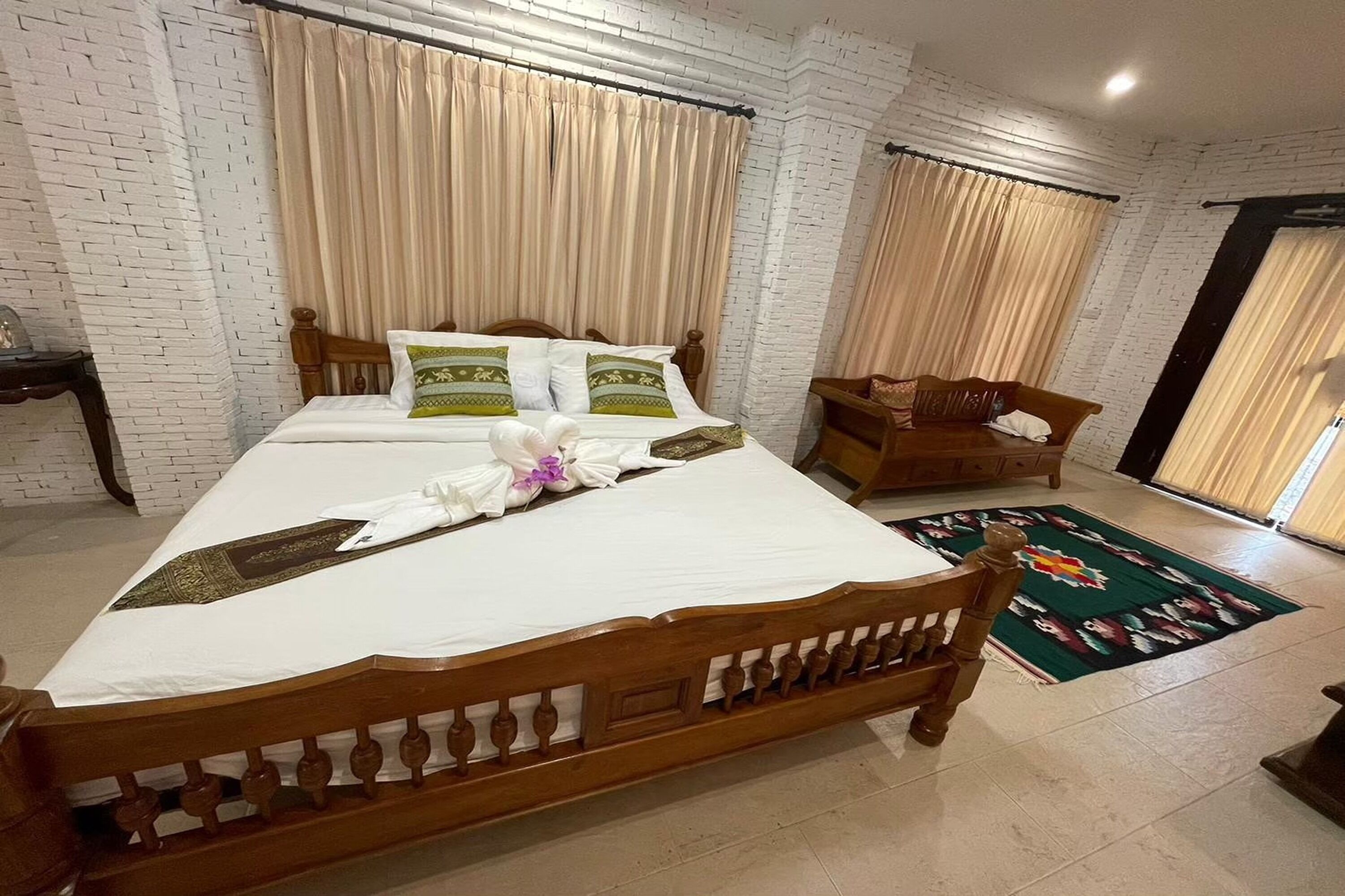 A neatly made bed with a white bedspread and decorative pillows, a wooden headboard, and a green patterned rug on the floor.