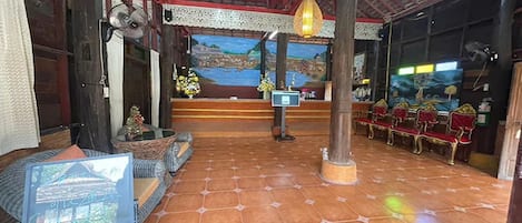 A traditional room with a tiled floor, a wooden ceiling, and a mural on the back wall. There are chairs and a small table with a vase of flowers.