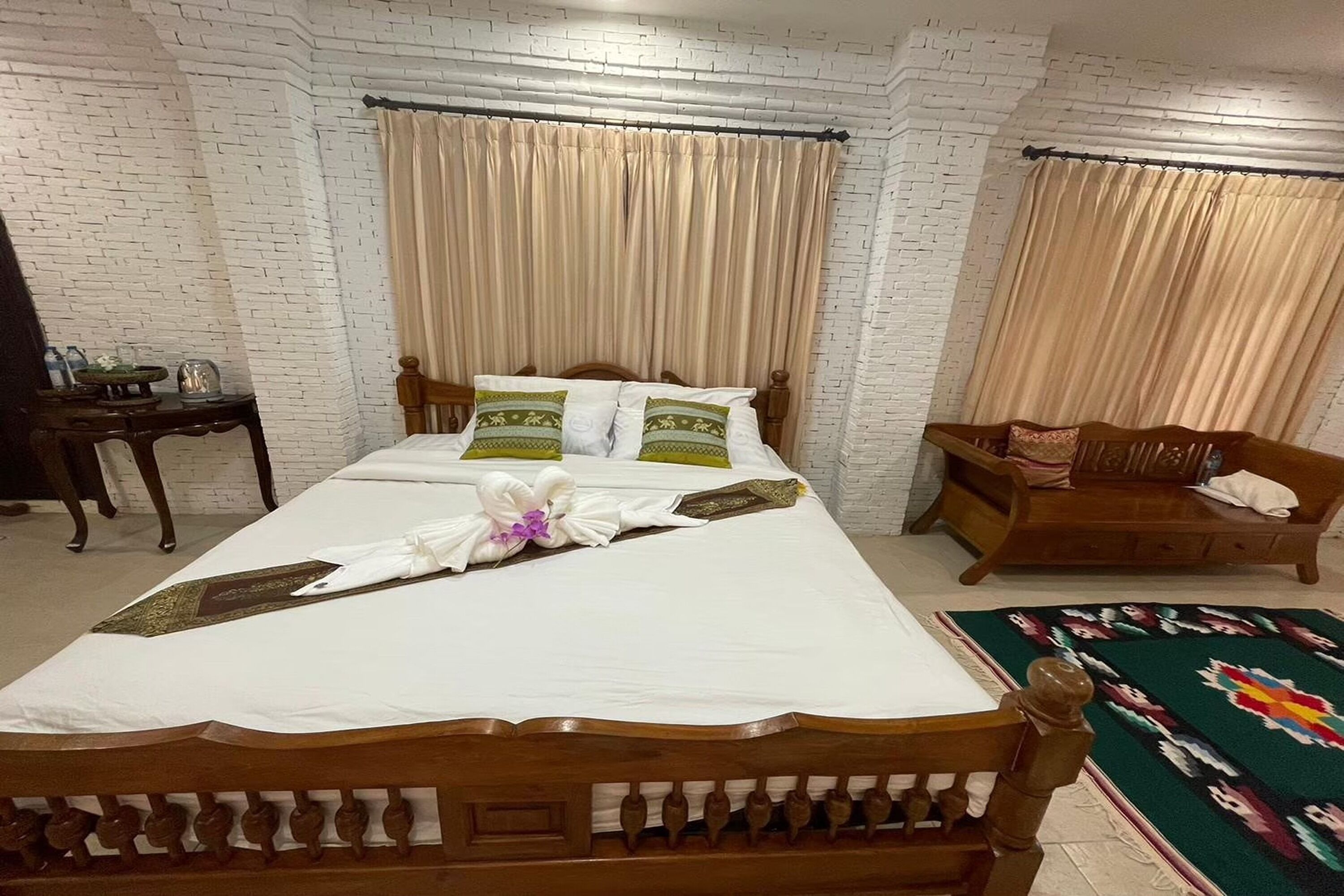 A neatly arranged hotel room with a large bed, a wooden nightstand, a small table, and a bench.