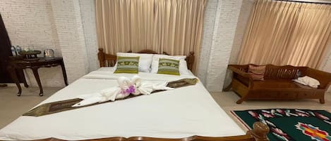 A neatly arranged hotel room with a large bed, a wooden nightstand, a small table, and a bench.