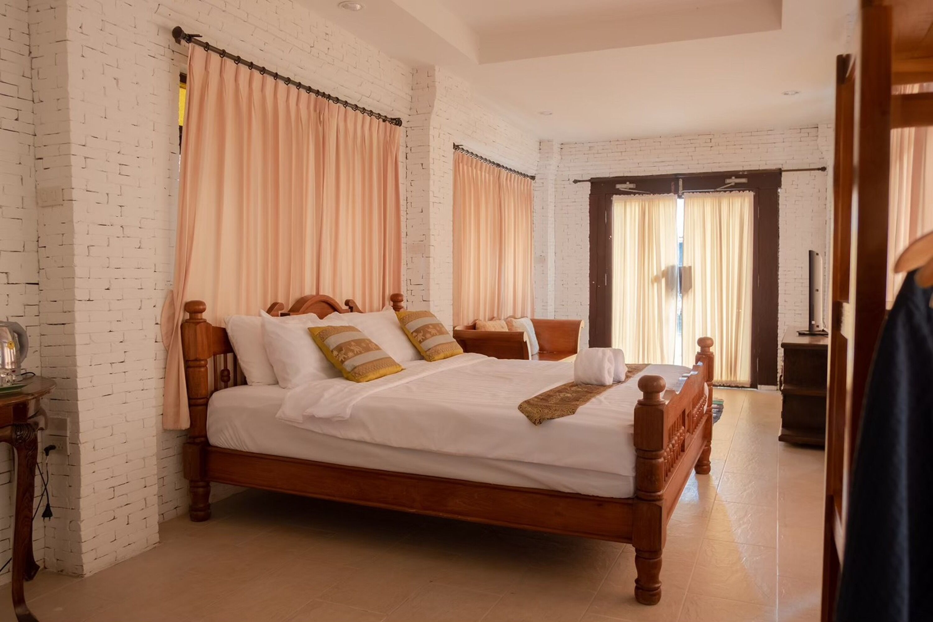 A neatly made bed with a wooden frame, a bedside table with a lamp, and a large window with curtains.