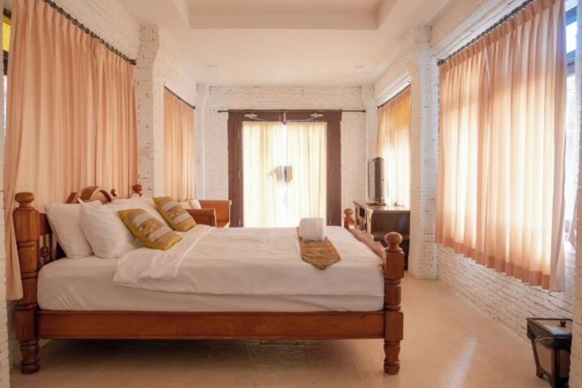 A neatly made bed with pillows and a blanket, a wooden headboard, and a small table with a lamp beside it.