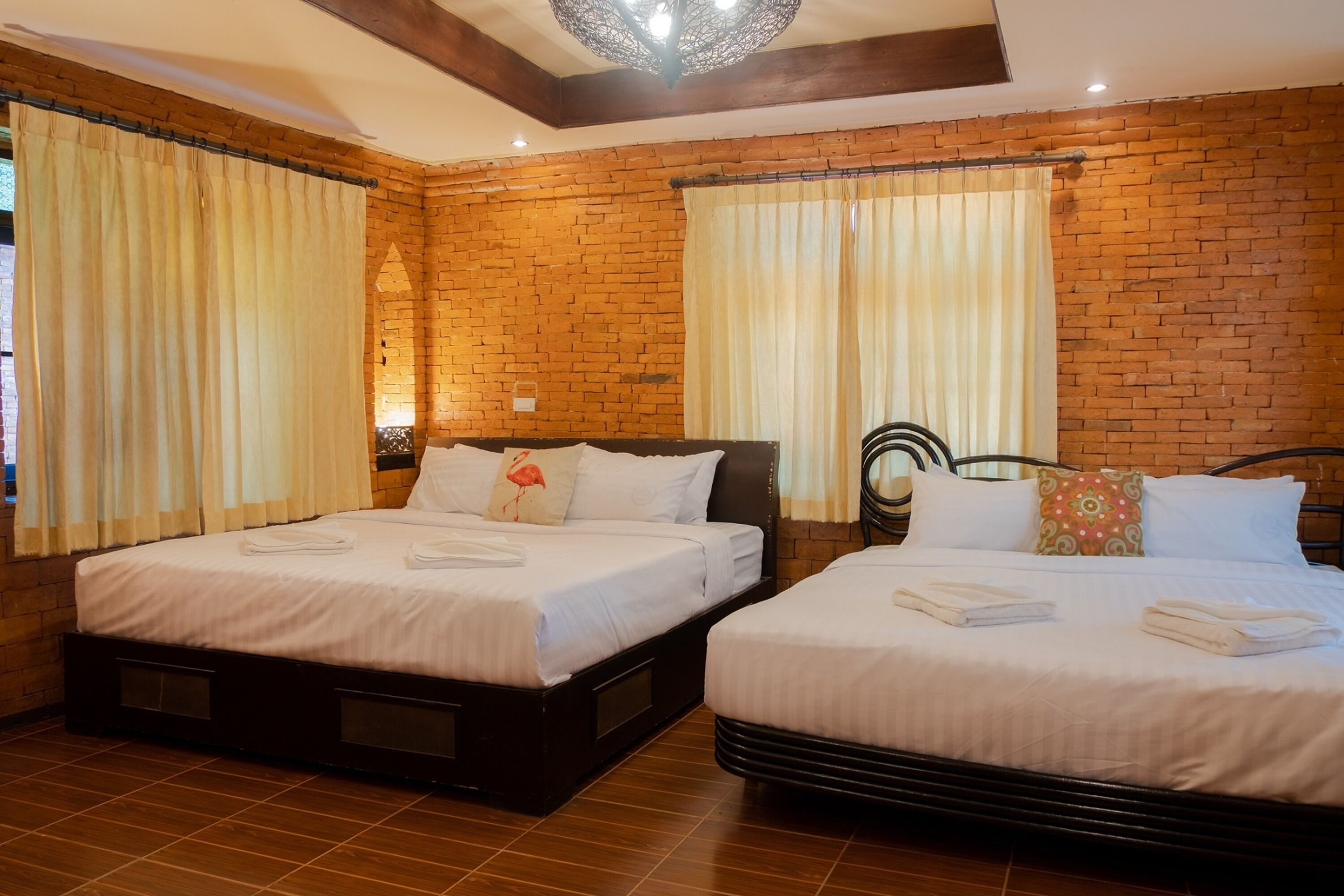A room with two beds, wooden floors, brick walls, and curtains.