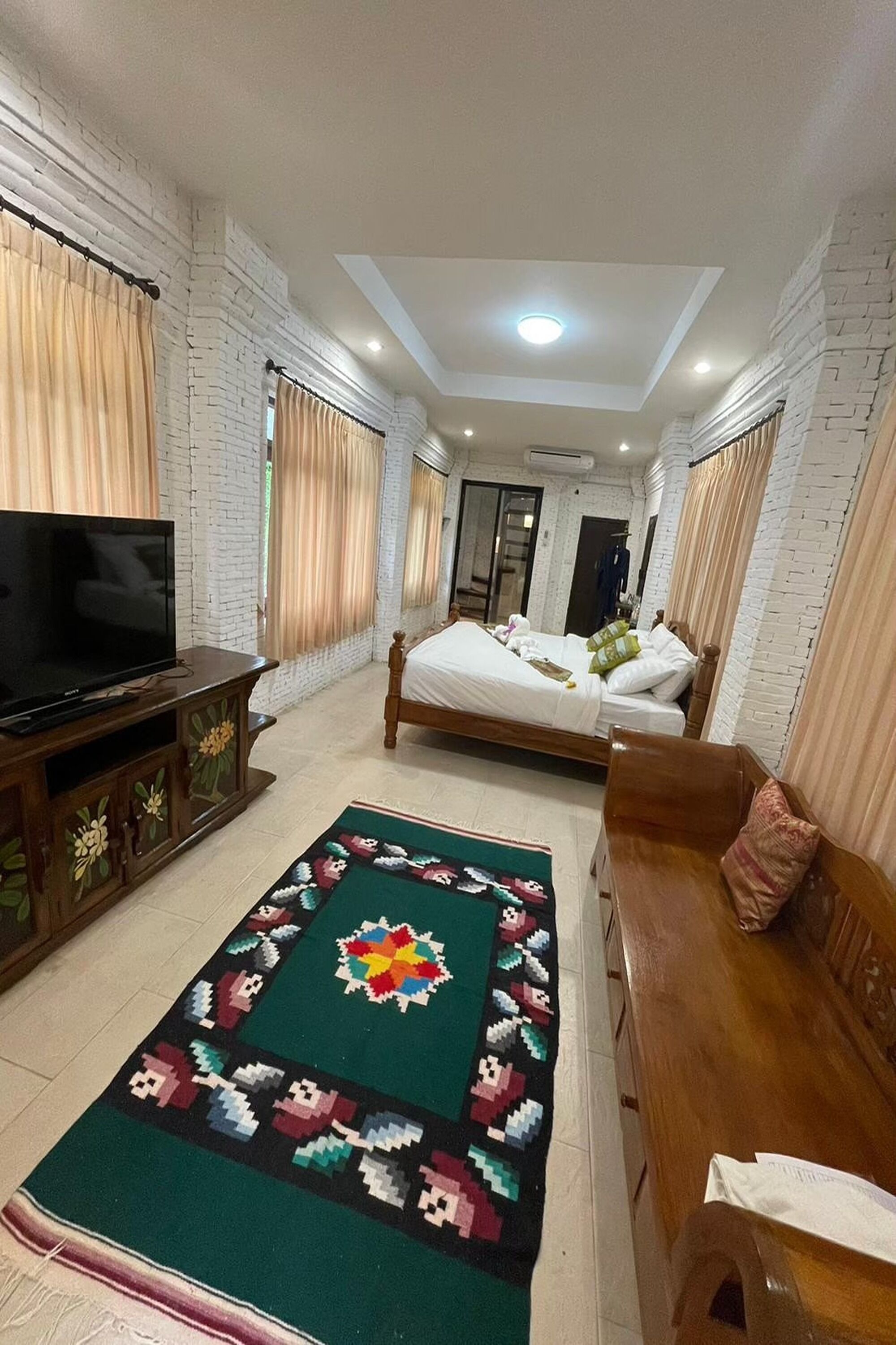 A hotel room with a bed, a TV, a wooden cabinet, and a colorful rug.