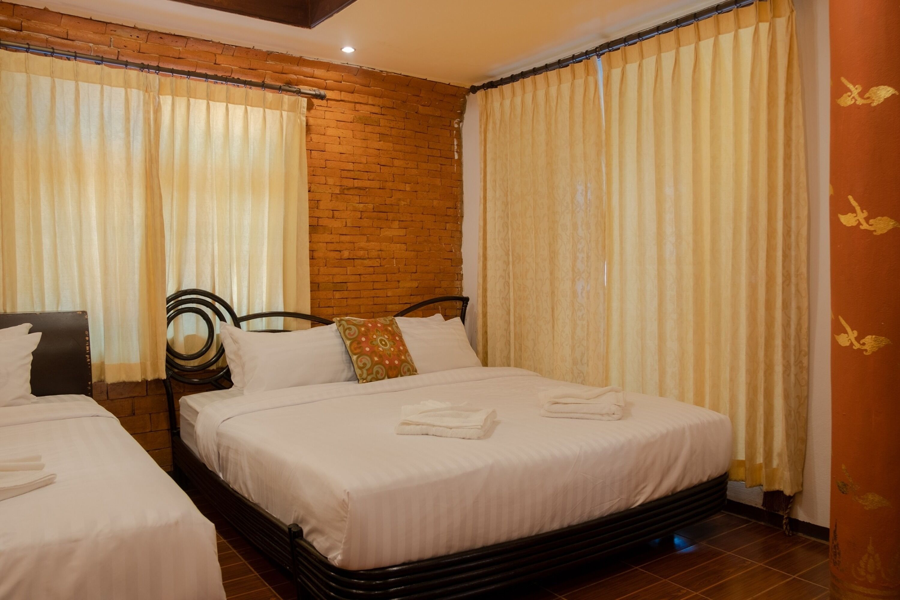 A hotel room with two beds, a brick wall, and curtains.