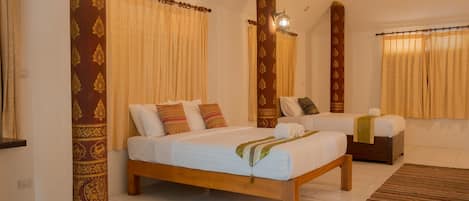 Une chambre d’hôtel avec un grand lit, un lit plus petit et un coin salon. Les fenêtres sont dotées de rideaux et il y a une lampe fixée au mur.