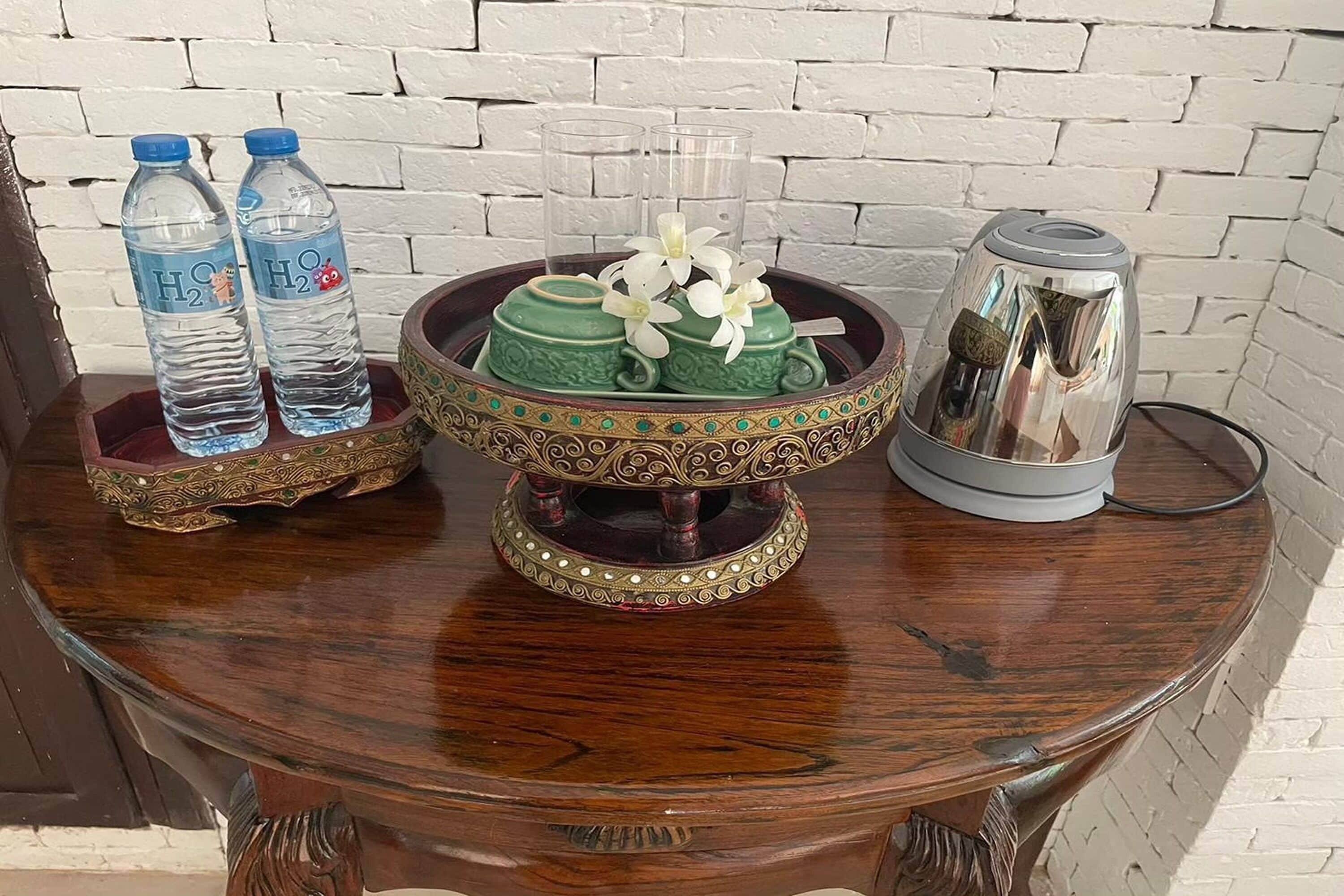 Une table en bois sur laquelle se trouvent un bol décoratif, deux bouteilles d’eau, un verre et une théière en argent.