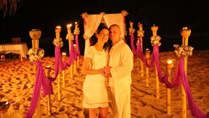 A couple standing under a canopy on a sandy beach at night, with decorative candles and flowers. - Arcade Beach Hotel (Induruwa)