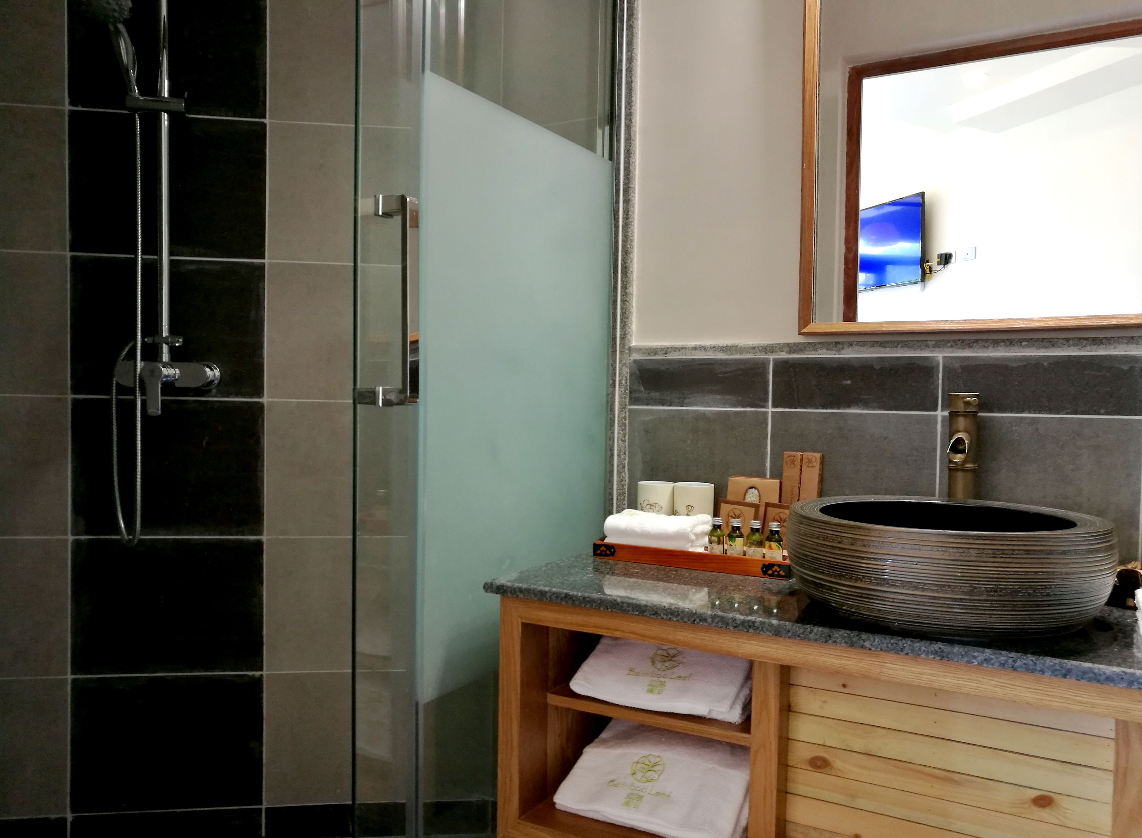 A bathroom with a glass shower enclosure, a sink with a large basin, and a wooden vanity with a towel rack.
