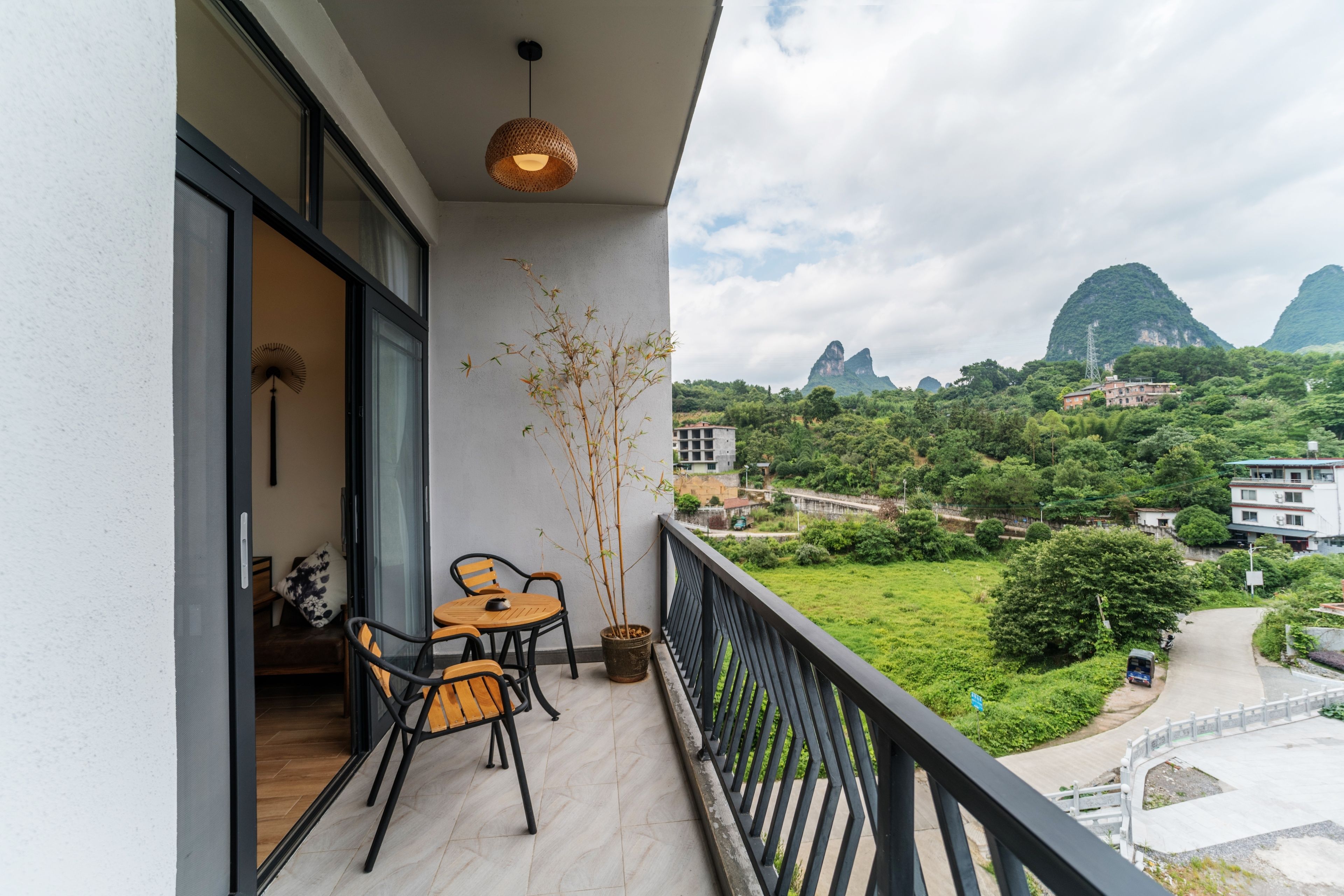 A balcony with a table and chairs, a potted plant, and a view of green hills and buildings.