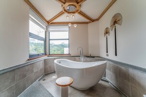 Un baño moderno con una bañera independiente, una ventana con vistas a la vegetación y un techo de madera.