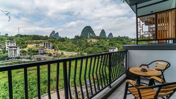 A balcony with a table and chairs, overlooking a green landscape and buildings.