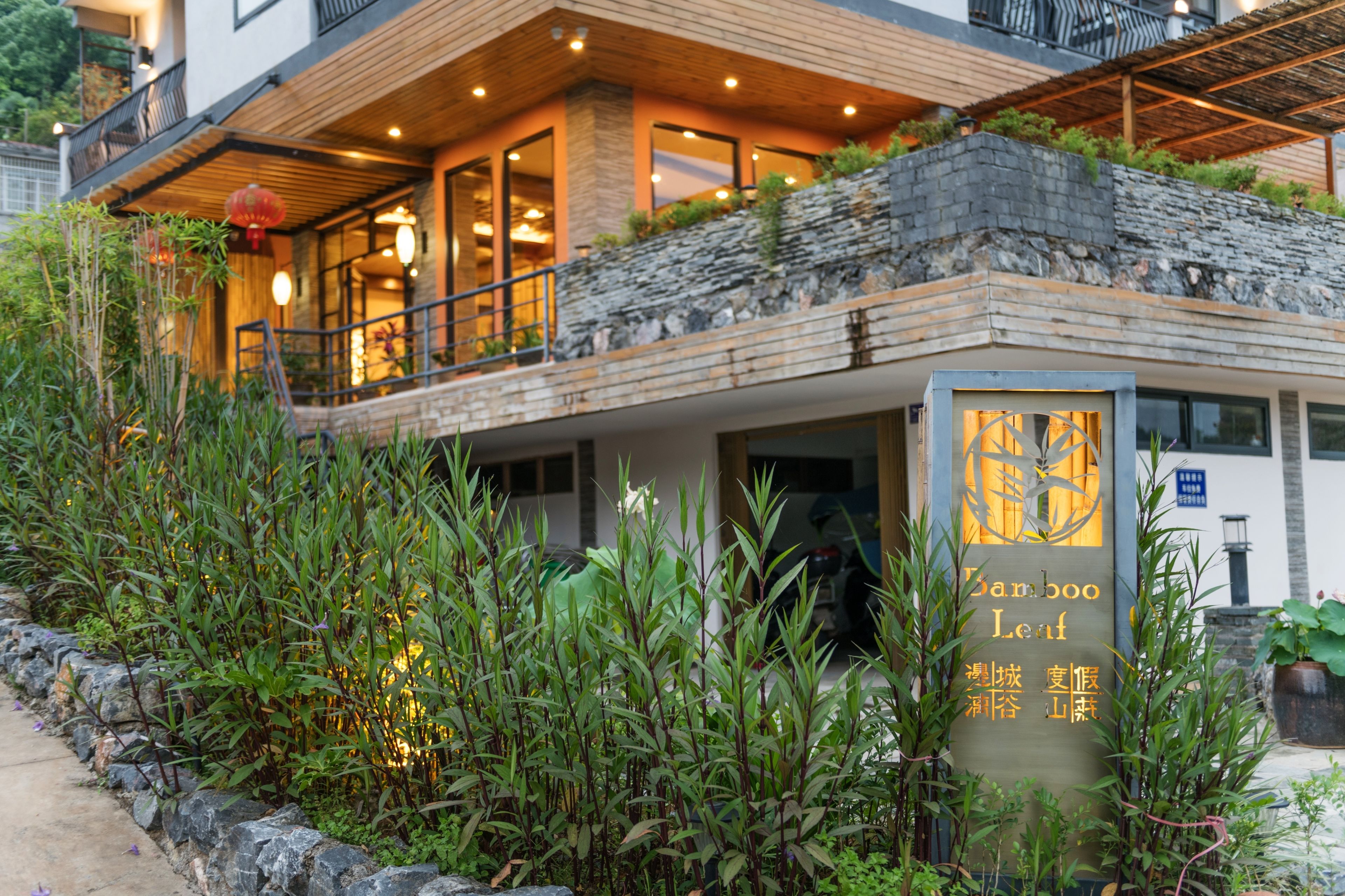 A modern building with a bamboo leaf sign, stone steps, and a balcony with plants.