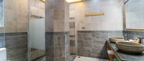 Une salle de bain moderne avec une douche à l’italienne en verre, un meuble-lavabo en bois doté de deux grands bacs et un miroir au-dessus du lavabo.