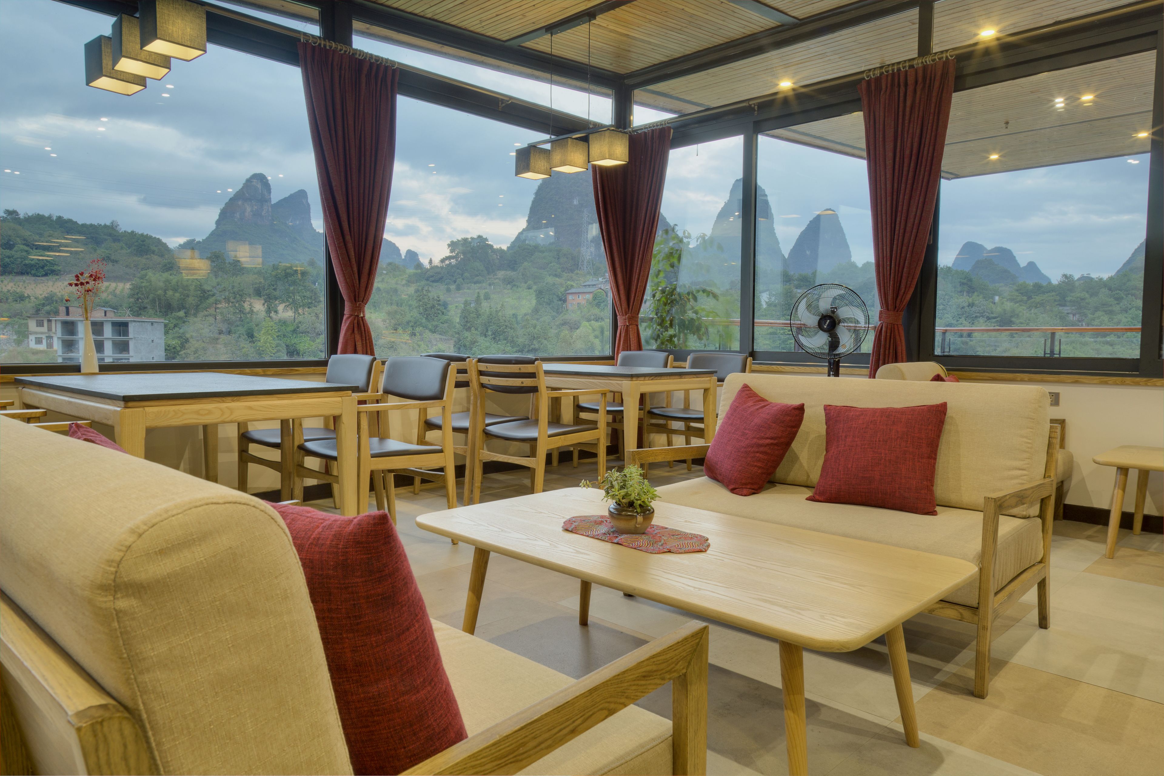 A modern dining area with wooden furniture, a fan, and a view of mountains.